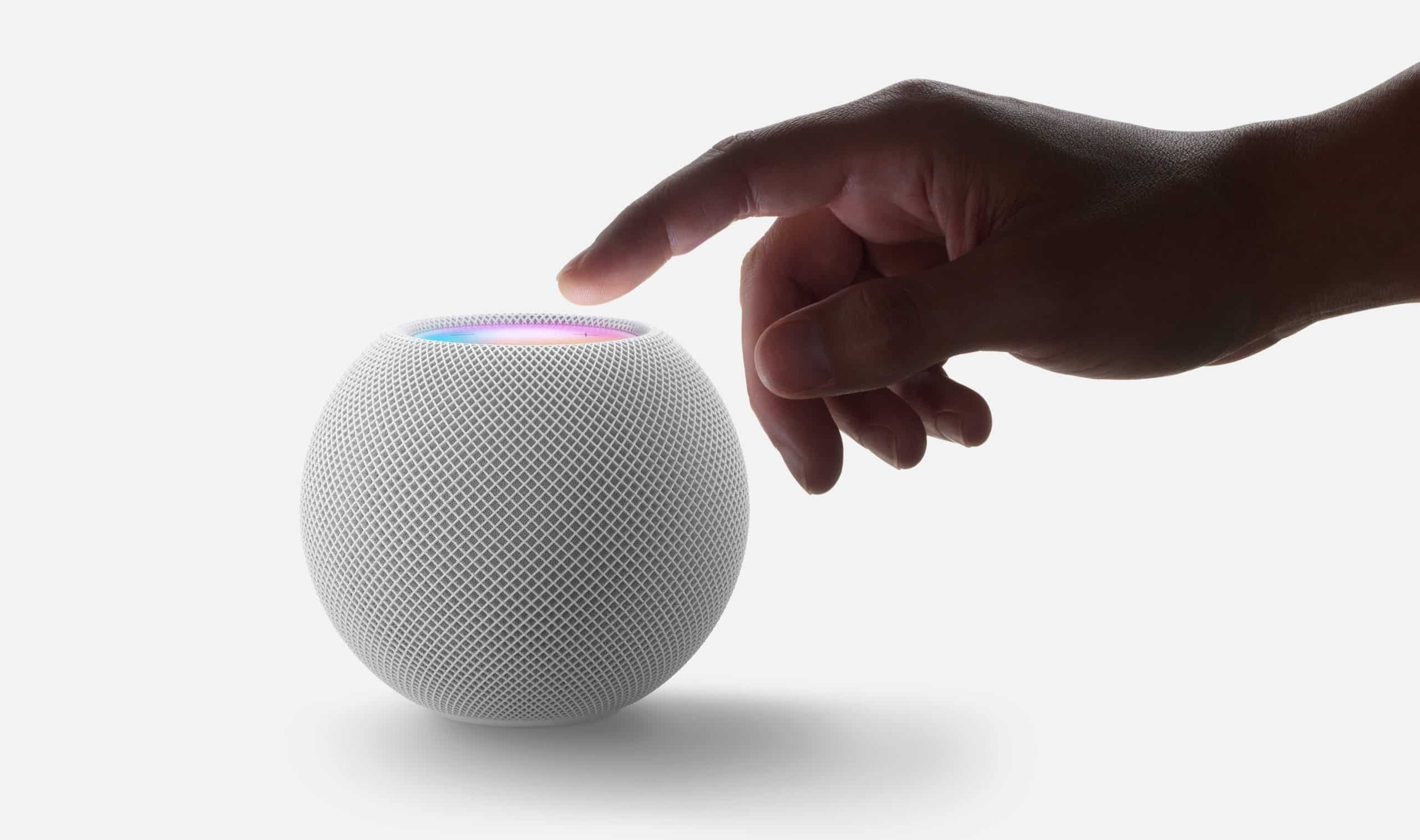 En hand når mot en vit HomePod mini med en lysande topp som indikerar röststyrning och beröringskontroll.