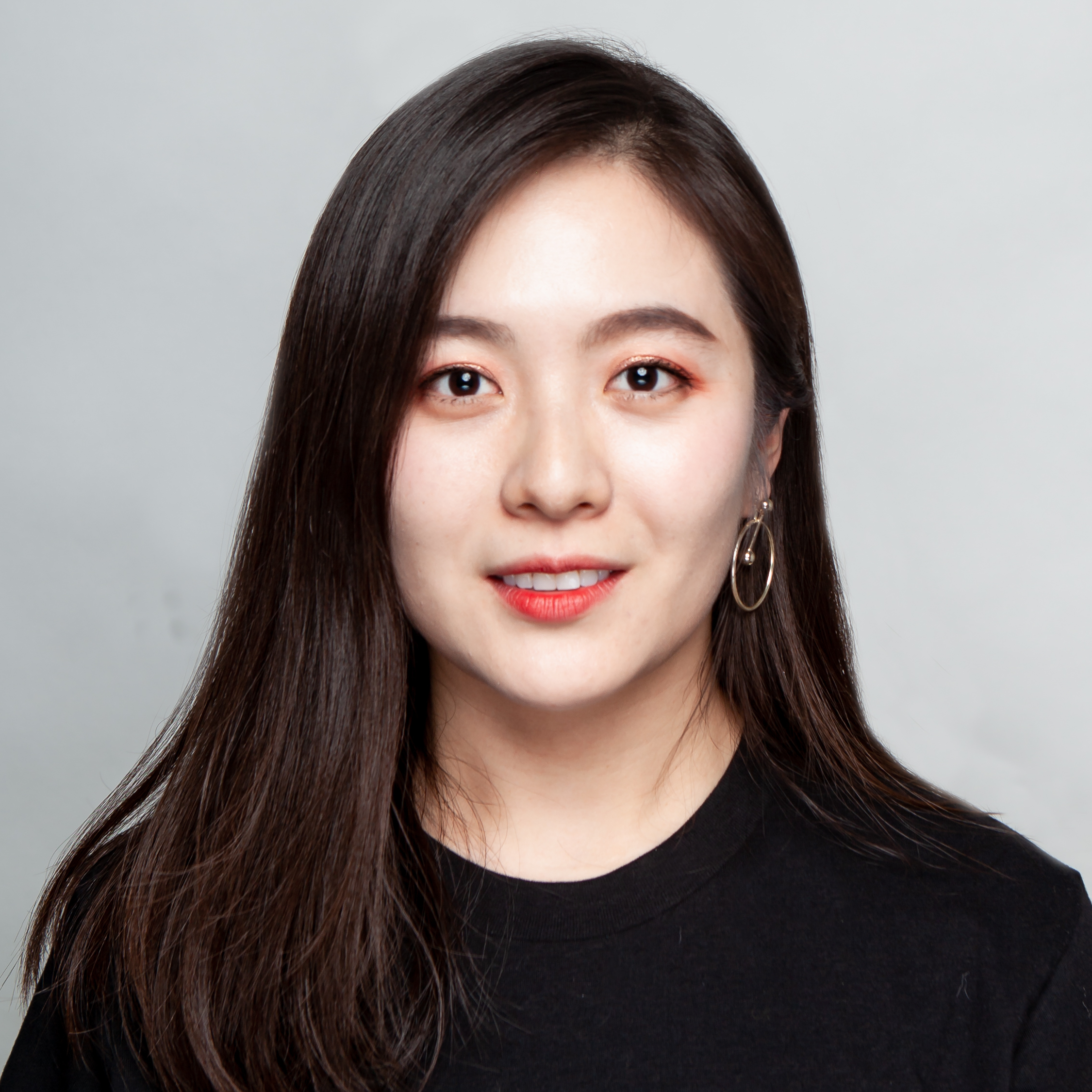 Xinyi Zhang smiles facing the camera directly. She is wearing a black boatneck top, red lipstick and hoop earrings.