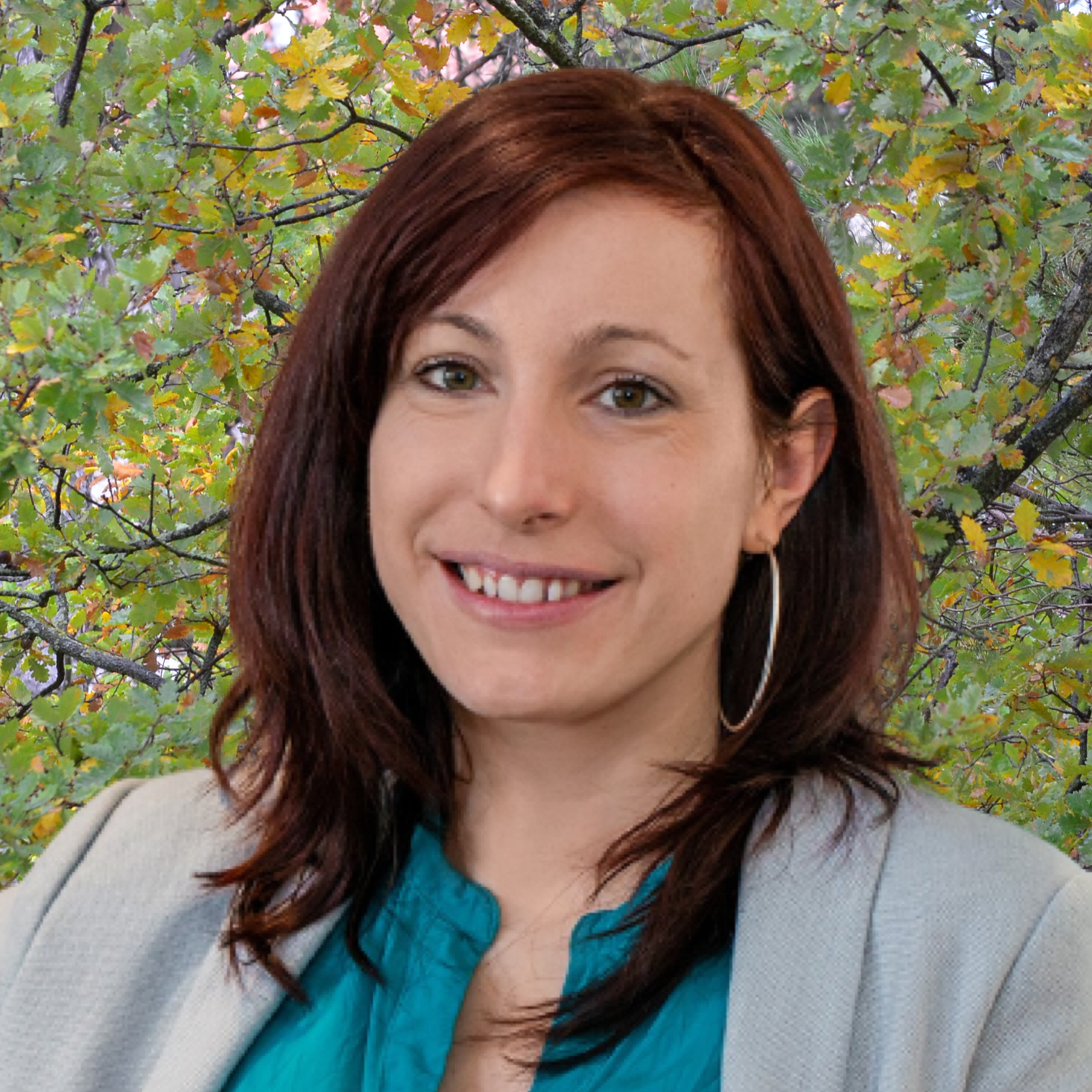 Lucie Gattepaille smiles with her head slightly tilted to the right. She is wearing a blue blouse with a light gray blazer and hoop earrings.