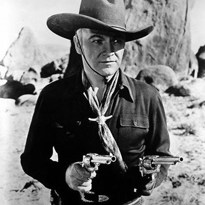 black and white photo of William Boyd as Hopalong Cassidy wearing a cowboy hat and holding two guns