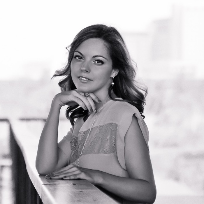 Agnieszka Wilk stands on a bridge. Her right elbow rests on the bridge's hand rail and her right hand rests underneath her chin. Her left hand sits atop the hand rail.
