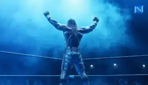 A muscular wrestler with flowing hair raises his arms in triumph under blue lighting, celebrating in the ring surrounded by fog.