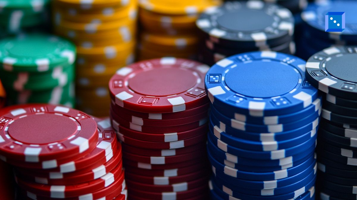 A close-up view of colorful casino chips stacked in piles, including red, blue, green, black, and yellow chips. The image conveys a sense of high-stakes gambling, wealth, and the casino environment.