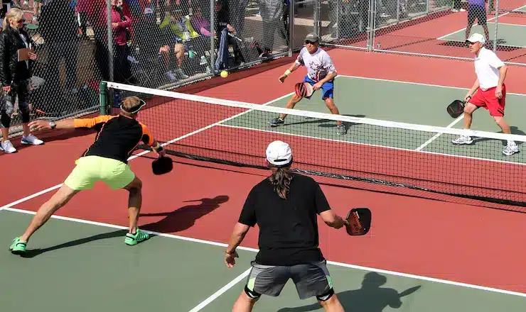 A dynamic pickleball match in progress, featuring four players actively competing on a vibrant court with spectators watching.