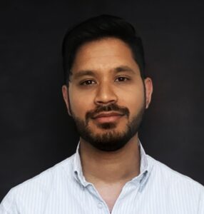 A Bivu Das wearing a light blue collared shirt stands against a dark background, showcasing a neutral expression.