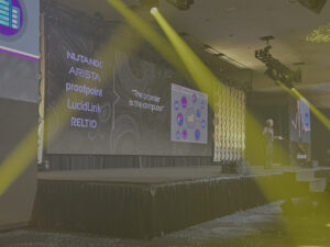 Mark Templeton presents on stage at a conference, with a lit backdrop displaying names of tech companies and a quote about browsers.