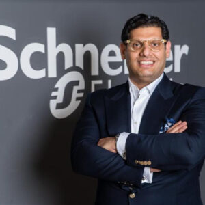 A well-dressed Michael Lotfy Gierges stands confidently with arms crossed, set against a Schneider Electric backdrop.