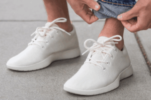 Man wearing white Allbirds sneakers tying laces on casual shoes outdoors close-up sustainable wool footwear minimalist style. Allbirds AI Pivot Runs Into Limits Of Capital And Experience