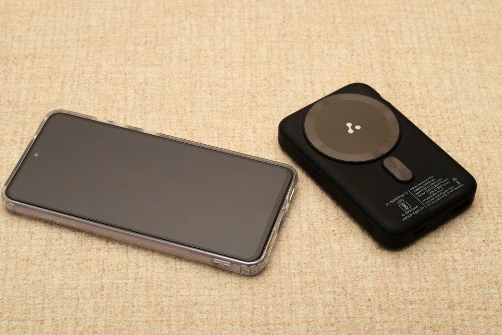 A smartphone next to a portable magnetic power bank on a light-colored surface