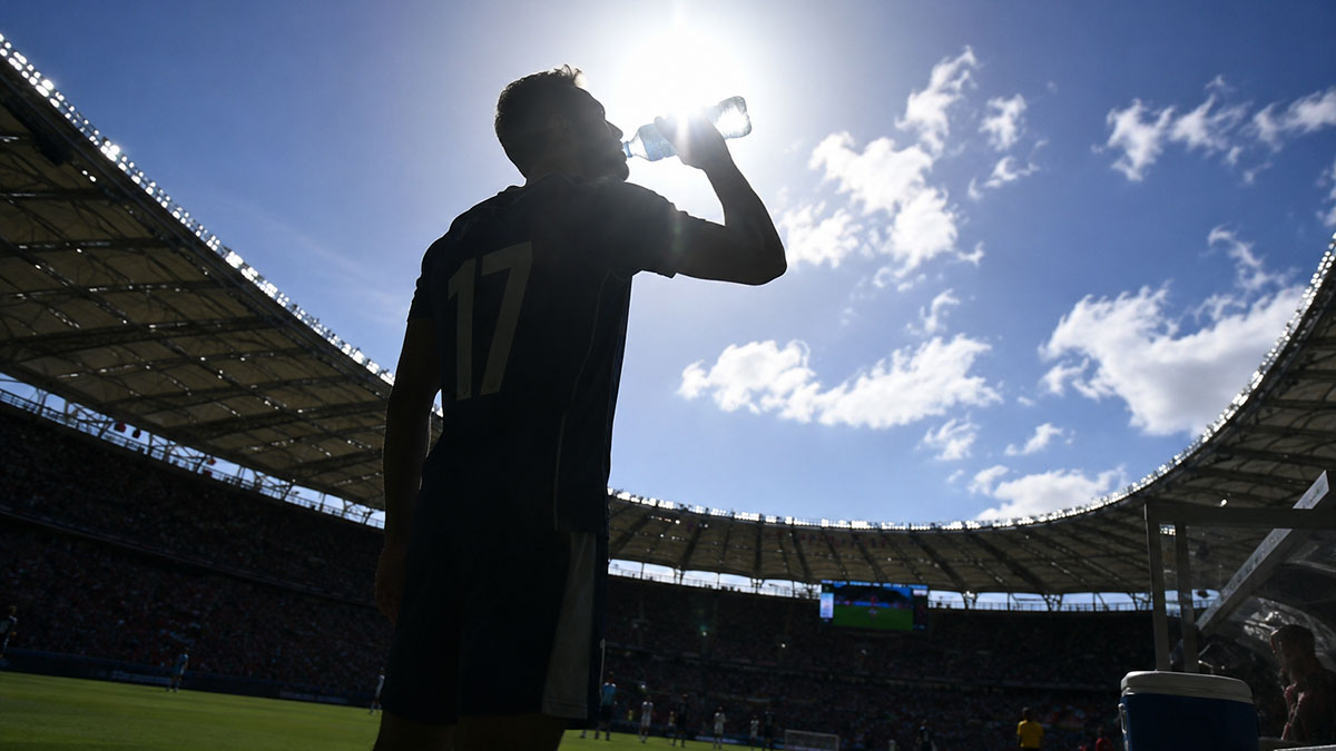 A soccer player drinks water on the sidelines.